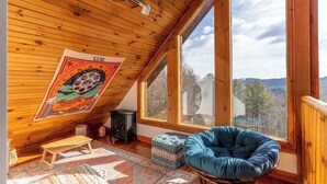 A cozy room with wooden ceiling, large windows, a blue bean bag chair, a small wooden bench, and a tapestry. - New River Retreat (Boone)