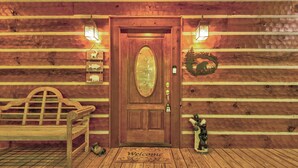 A wooden cabin entrance with a bench, a welcome mat, and a bear statue. - Hebron Falls (Boone)
