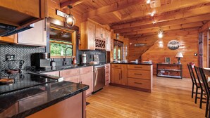A wooden cabin interior with a kitchen featuring a herringbone tile backsplash, wooden cabinets, and a black countertop. - Come to Escape (Marion)