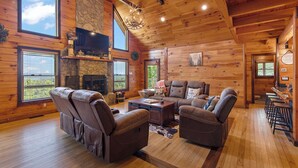 A log cabin interior with a fireplace, leather sofas, a TV, and large windows. - Come to Escape (Marion)