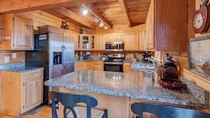 A spacious kitchen with granite countertops, wooden cabinets, stainless steel appliances, and a large island with bar stools. - Atop Boone (Boone)