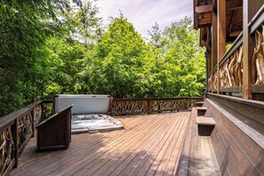 En træterrasse med et spabad og siddeområde, omgivet af frodig vegetation.