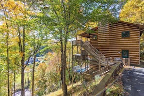 Eine Holzhütte mit einer Treppe zu einer Terrasse, umgeben von Herbstlaub.