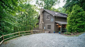 A rustic cabin with a stone chimney, a wooden deck, and a gravel driveway. - Among The Trees (Vilas)