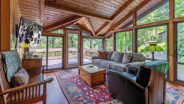 A spacious living room with a wooden ceiling, large windows, a sofa, a coffee table, and a television. - A River Mist (Sugar Grove)