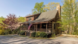 A rustic log cabin with a stone chimney, a porch with a railing, and an American flag. - Altitude Adjustment (Banner Elk)