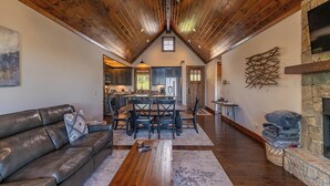 A spacious living area with a high wooden ceiling, a fireplace, a dining table with chairs, and a kitchen in the background. - Kikis Hideaway at Eagles Nest (Banner Elk)