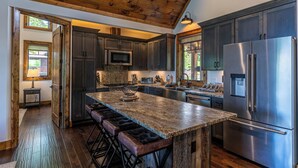 A kitchen with dark wood cabinets, a stainless steel refrigerator, a granite countertop, and a wooden island with bar stools. - Kikis Hideaway at Eagles Nest (Banner Elk)