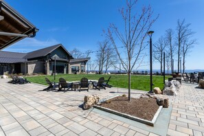 A patio area with outdoor seating, a stone fireplace, and a view of a building with a modern architectural style. - Craig 201 Jurassic (Lenoir)