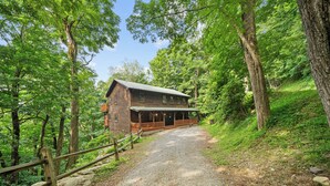A wooden cabin with a porch, surrounded by trees and a gravel path. - Acorn Lodge (Banner Elk)