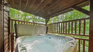 A hot tub on a wooden deck with a railing, surrounded by trees. - Acorn Lodge (Banner Elk)