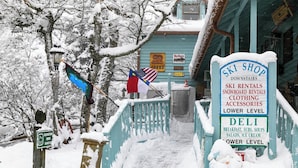 Un espace extérieur enneigé avec une enseigne indiquant un magasin de ski, où l’on peut louer du matériel et acheter des vêtements.