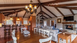 A spacious living room with a large wooden dining table, white chairs, a grey sofa, and a fireplace. - Emerald Escape (Banner Elk)