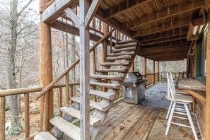Una escalera de madera que lleva a una terraza con mobiliario exterior y una parrilla.