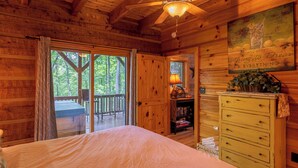 A wooden cabin bedroom with a bed, a dresser, a ceiling fan, and a view of the outdoors. - Walk In The Clouds (Boone)