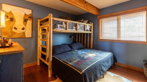 A bunk bed with a wooden ladder, a desk with a lamp, a framed animal painting, and a window with blinds. - Mountaineer Manor (Sugar Grove)