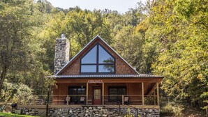 Eine Holzhütte mit einem Steinkamin, großen Fenstern und einer Veranda mit Sitzgelegenheit.