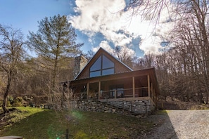 A cabin with a stone foundation, large windows, and a wooden deck. - A River Mist Walk (Sugar Grove)