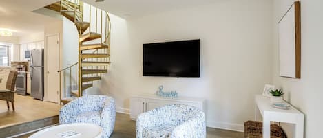 A modern living room with a spiral staircase, a flat-screen TV, and a small white console table.