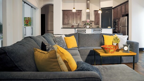Ein modernes Wohnzimmer mit einem grauen Ecksofa, gelben Kissen und einem Holztisch.