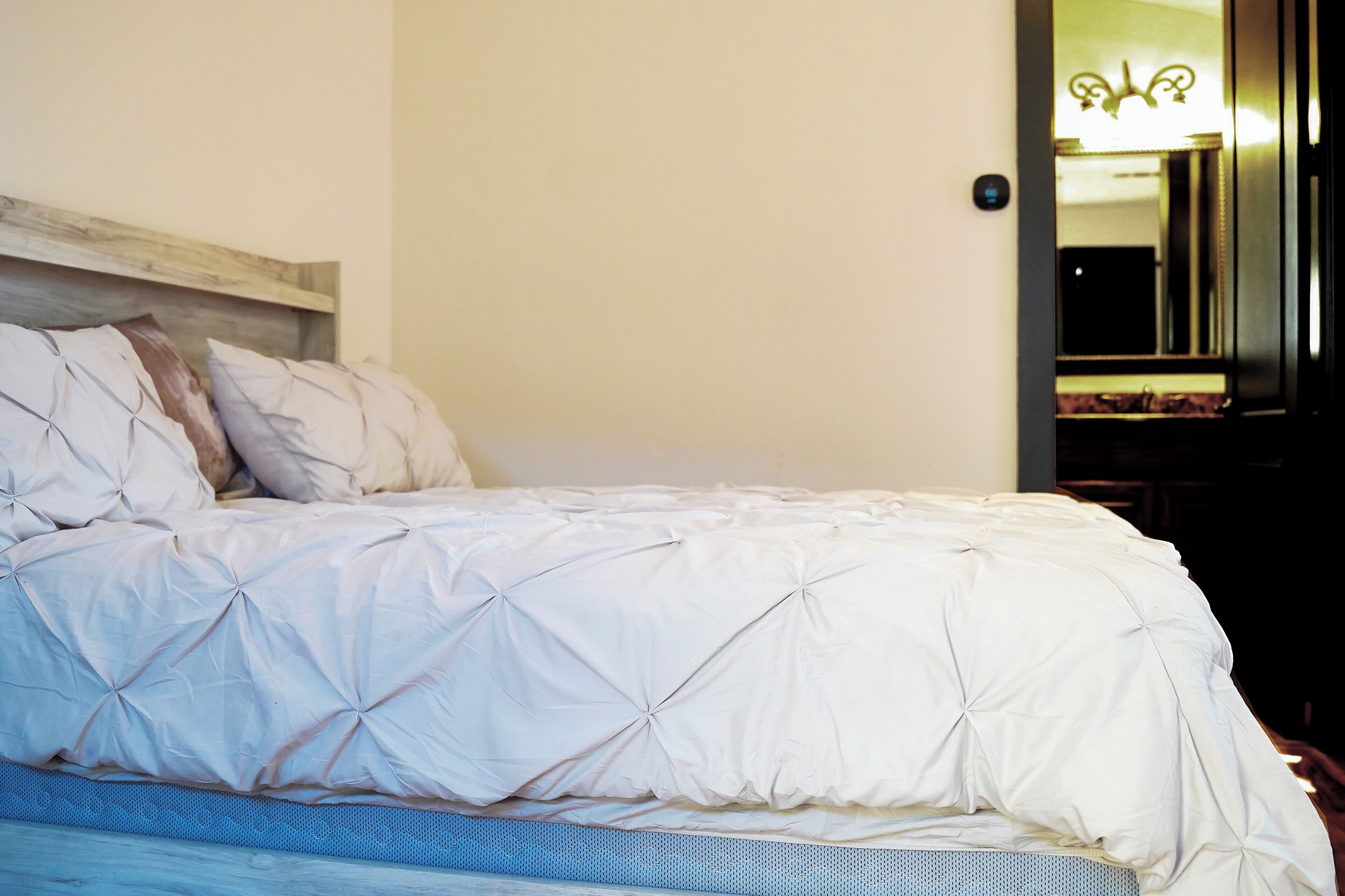 Un lit avec une couette et des oreillers blancs, une tête de lit en bois et un miroir au mur.