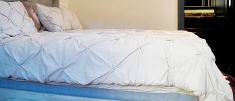 Un lit avec une couette et des oreillers blancs, une tête de lit en bois et un miroir au mur.