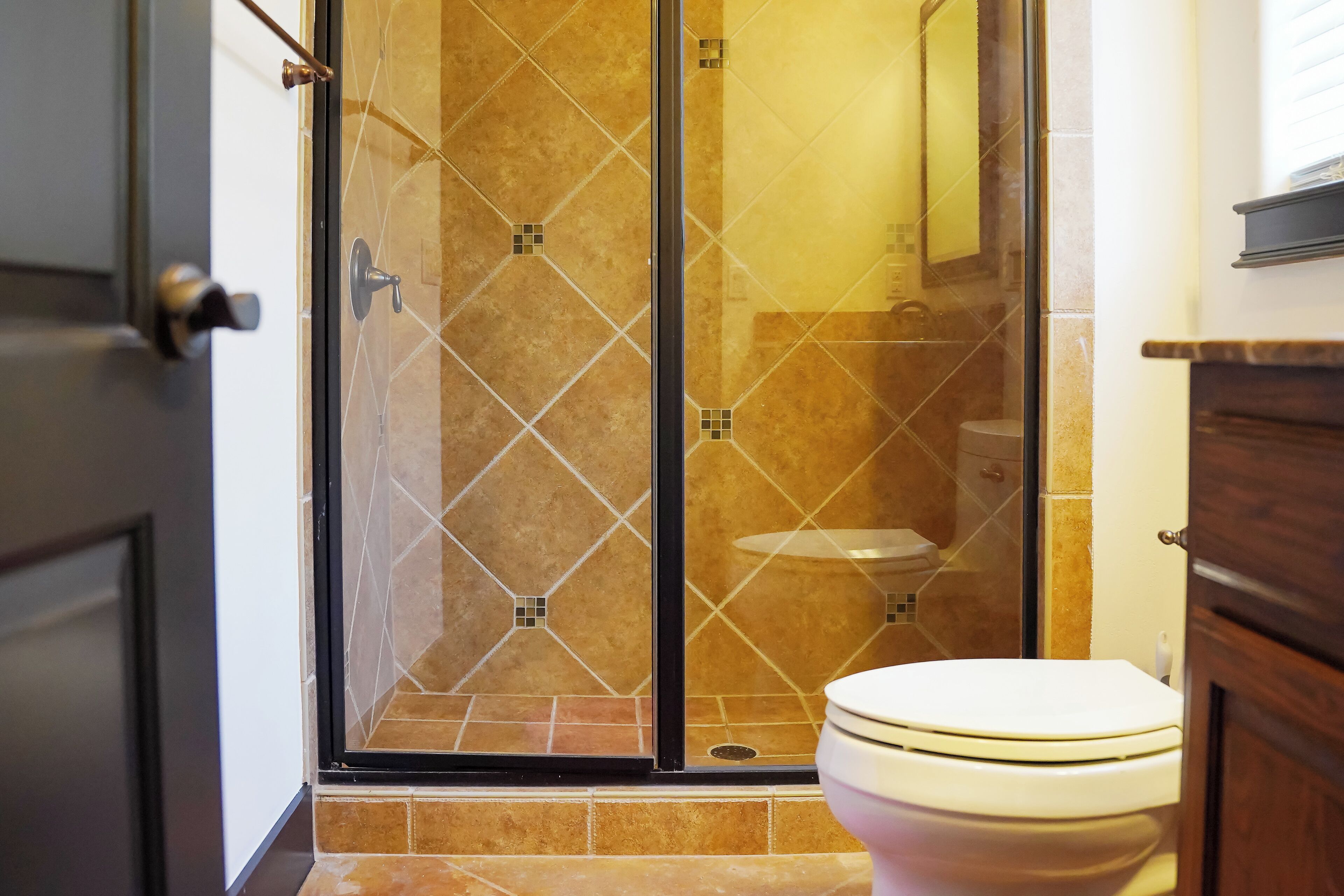 A bathroom with a glass-enclosed shower, a toilet, and a wooden cabinet.