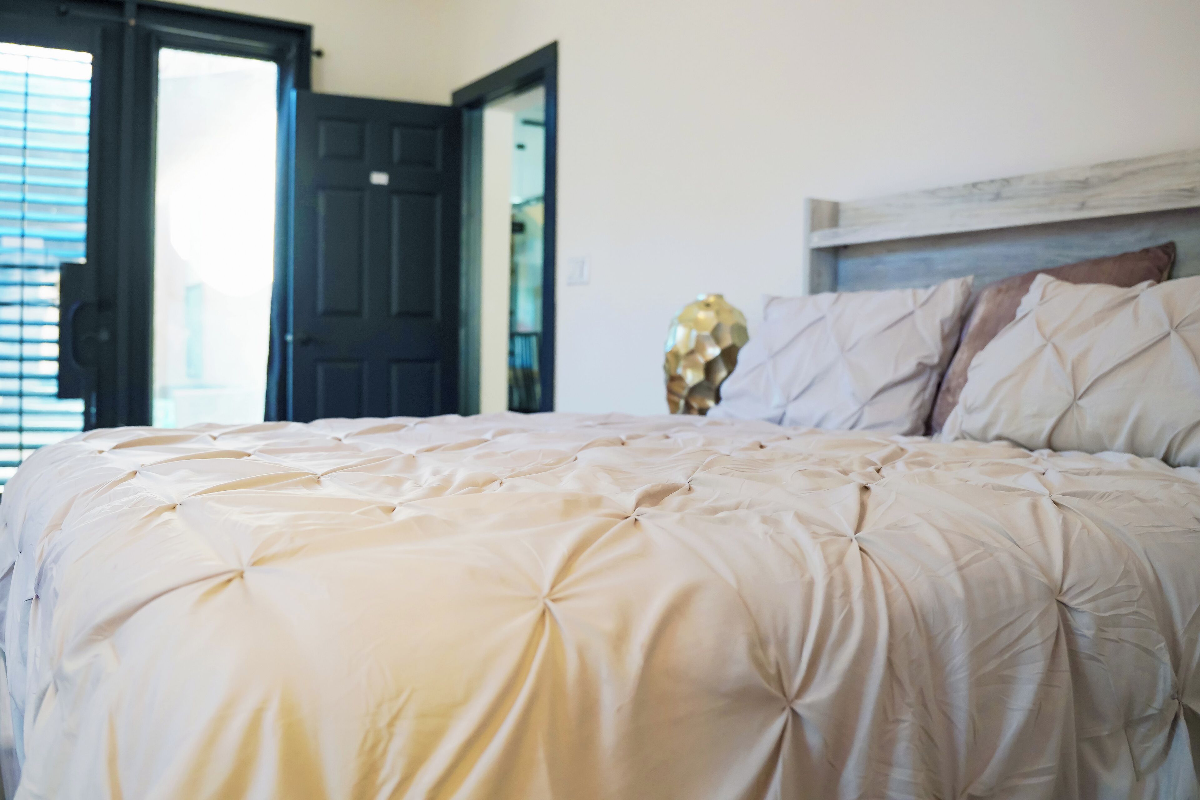 Een slaapkamer met een groot bed, een houten hoofdbord en een deur naar een andere kamer.