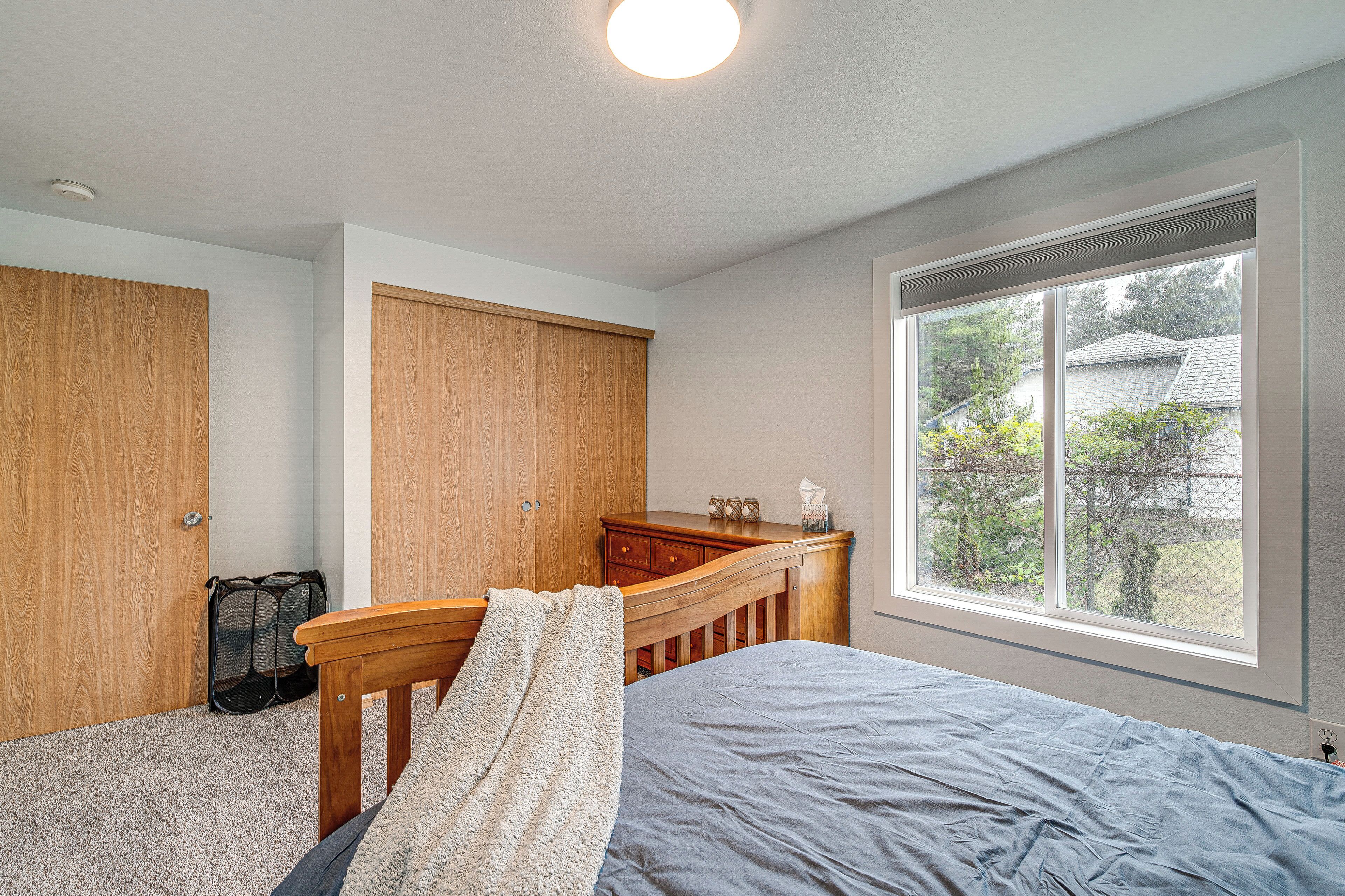 A bedroom with a bed, a wooden headboard, a window with a view of the outside, and a closet with a door.