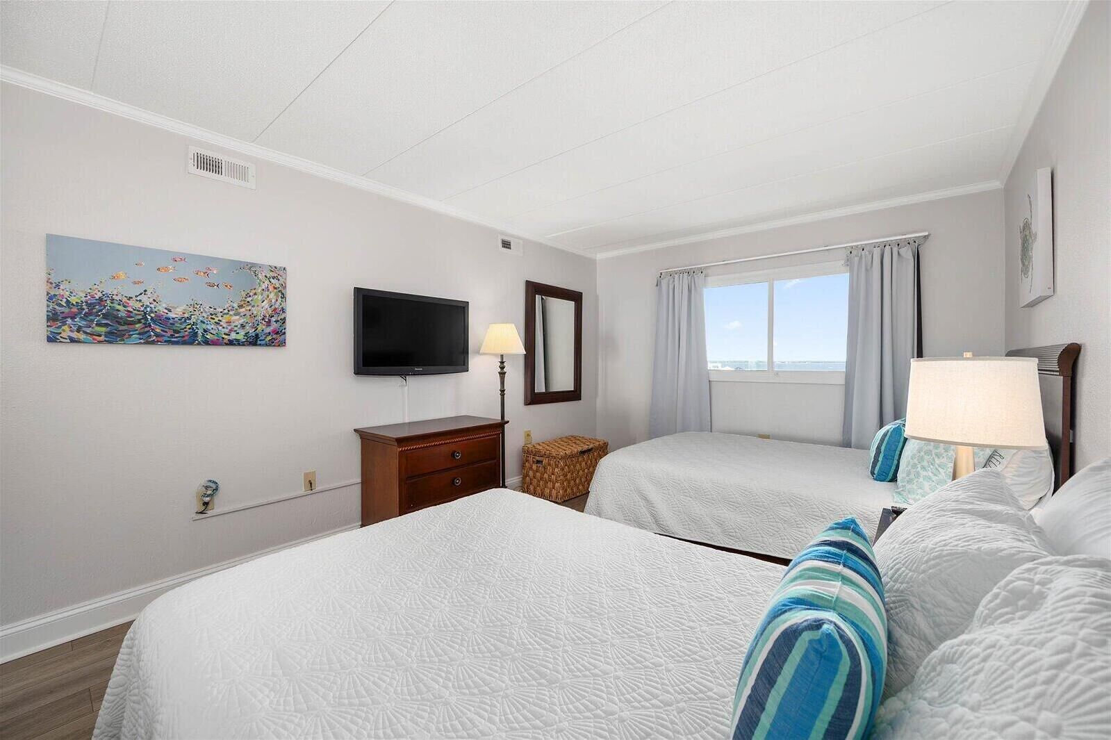 Une chambre d’hôtel avec deux lits, une télévision, une fenêtre avec des rideaux et un tableau au mur.