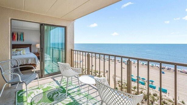 Un balcón con una cama, dos sillas, una mesa y vistas a la playa.