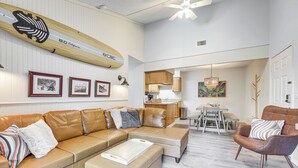 A modern living room with a sectional sofa, a coffee table, and a dining area with a chandelier. - Amelia Island Condo w/ Pool Access: Walk to Beach! (Fernandina Beach)