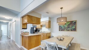A modern kitchen with wooden cabinets, a central island, and a dining area with a bench. - Amelia Island Condo w/ Pool Access: Walk to Beach! (Fernandina Beach)