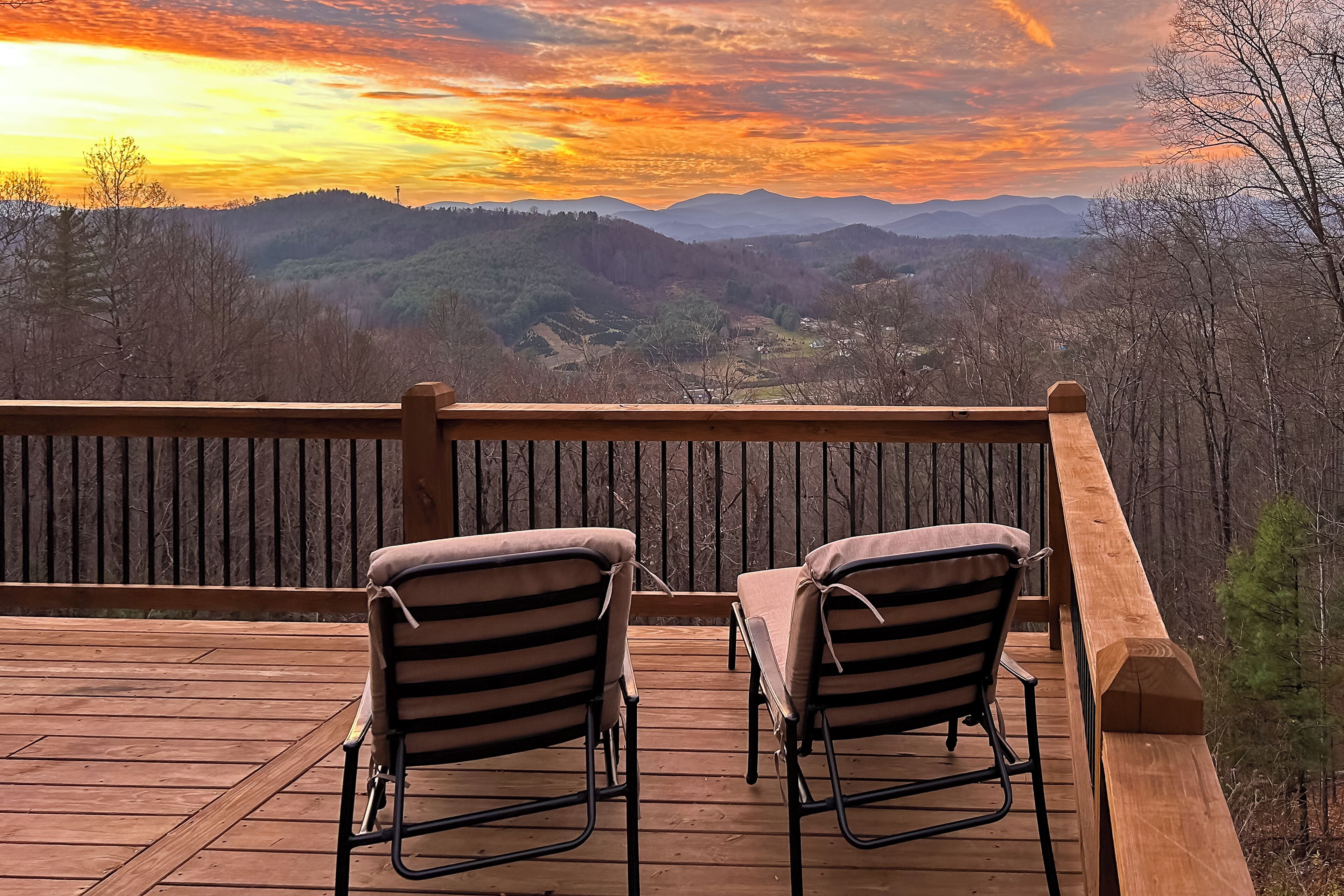A wooden deck with two striped chairs facing a scenic view of mountains and a sunset.