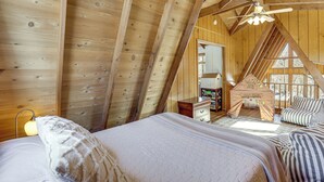 Una camera da letto mansardata accogliente, con soffitto spiovente, travi in legno, un letto con copriletto, un comodino, una cassettiera e una piccola casetta da gioco.