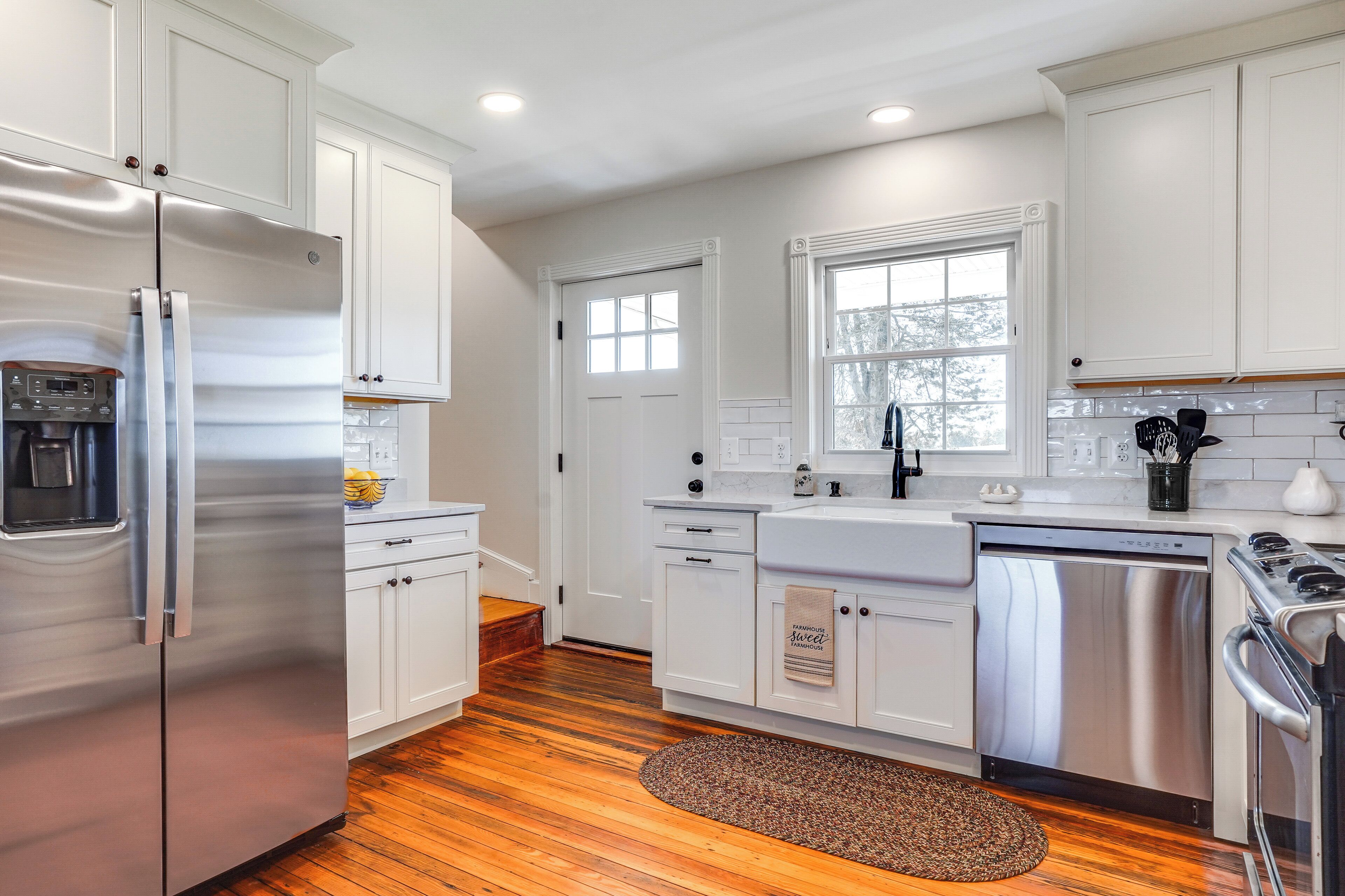 Una cocina moderna con armarios blancos, electrodomésticos de acero inoxidable y piso de madera.