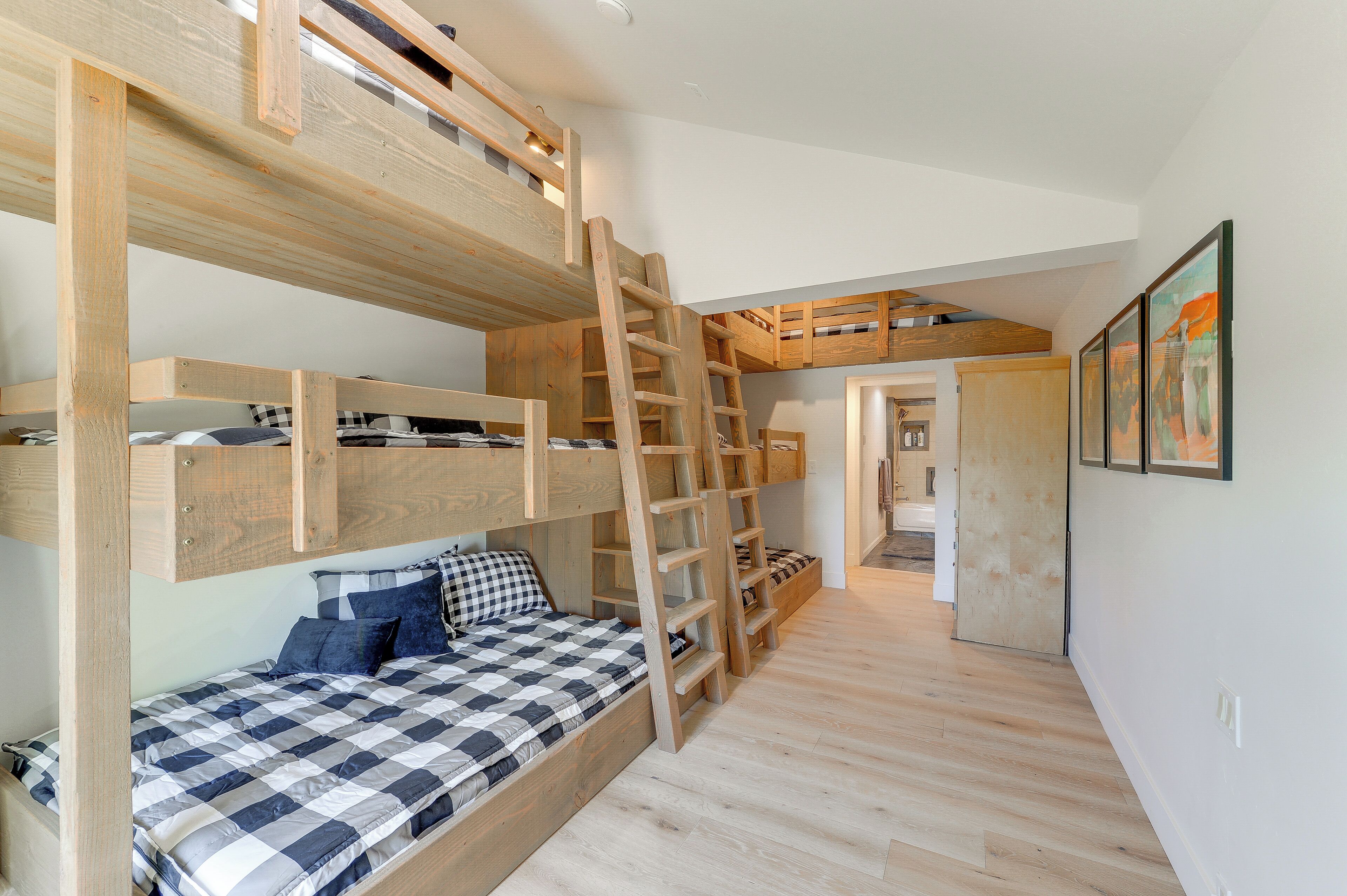 Dormitorio con literas, una escalera, una colcha a cuadros y un pasillo que conduce a otra habitación.