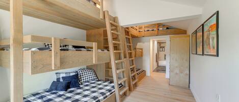 Dormitorio con literas, una escalera, una colcha a cuadros y un pasillo que conduce a otra habitación.