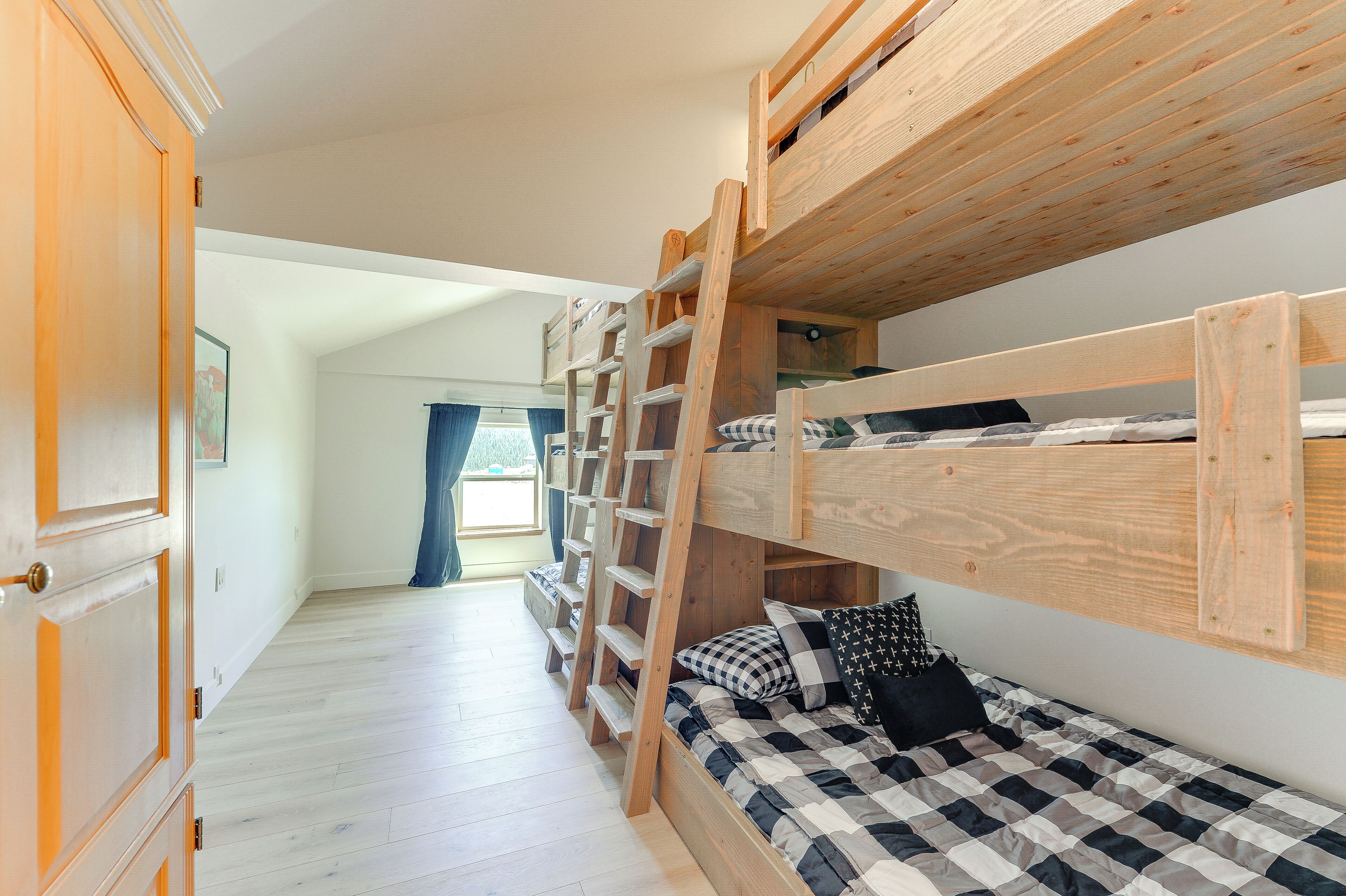 Dormitorio con literas, una escalera de madera, colcha a cuadros y un armario de madera.