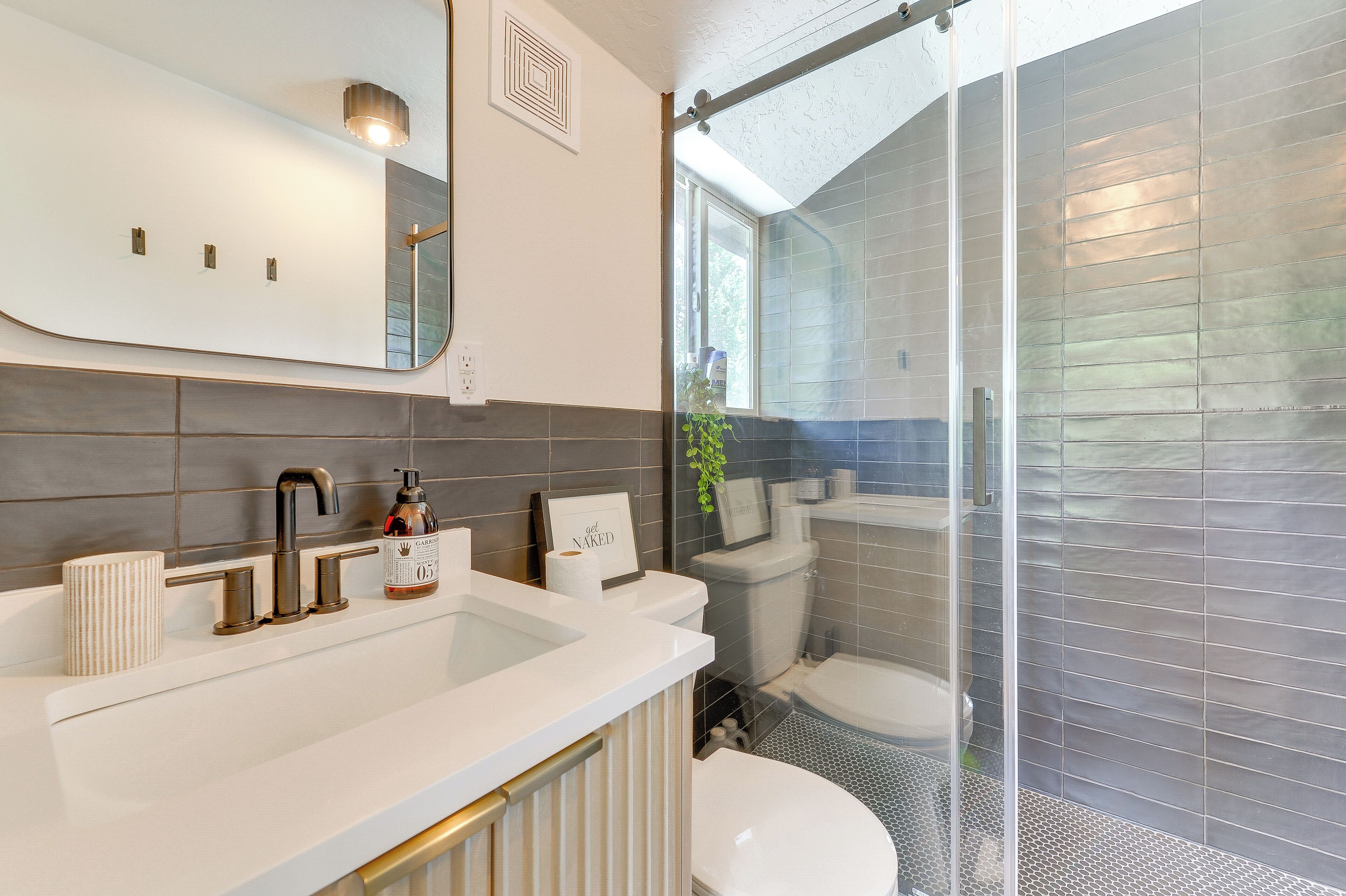 Een moderne badkamer met een grote spiegel, een witte wastafel met een gouden kraan en een douchecabine van glas.