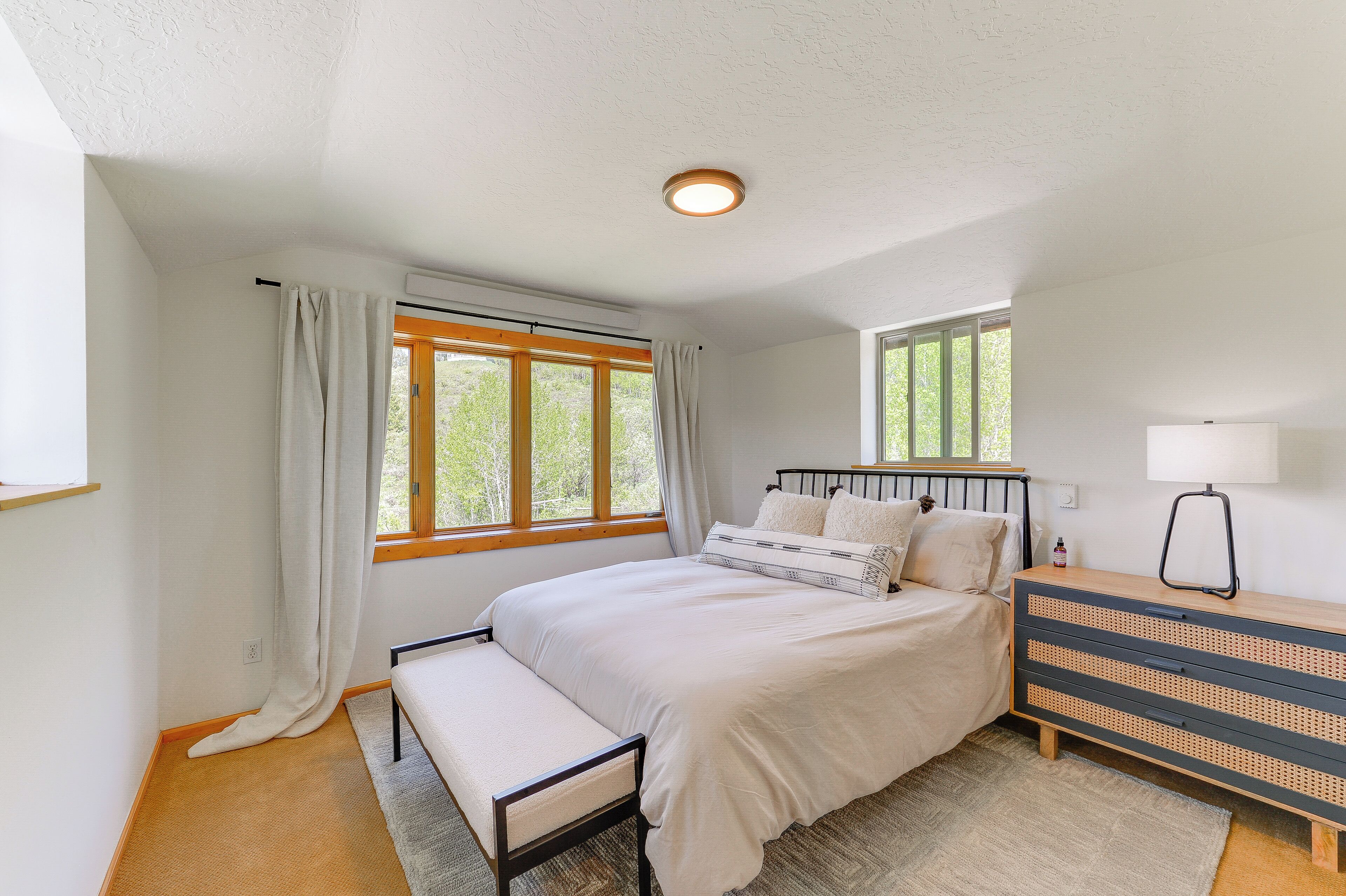 Een slaapkamer met een bed, een bankje, een kaptafel en een raam met gordijnen.