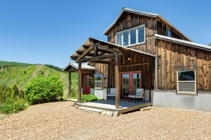 A rustic wooden house with a covered porch, large windows, and a view of a green hillside. - Salt River Access: Mtn-view Star Valley Cabin! (Thayne)