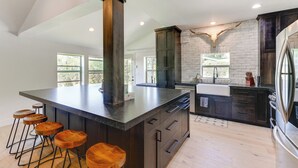 A modern kitchen with a large island, bar stools, dark cabinetry, and a stone accent wall. - Salt River Access: Mtn-view Star Valley Cabin! (Thayne)