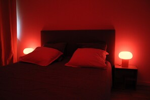 Ein schwach beleuchtetes Zimmer mit einem Bett, zwei Nachttischen und rotem indirektem Licht.