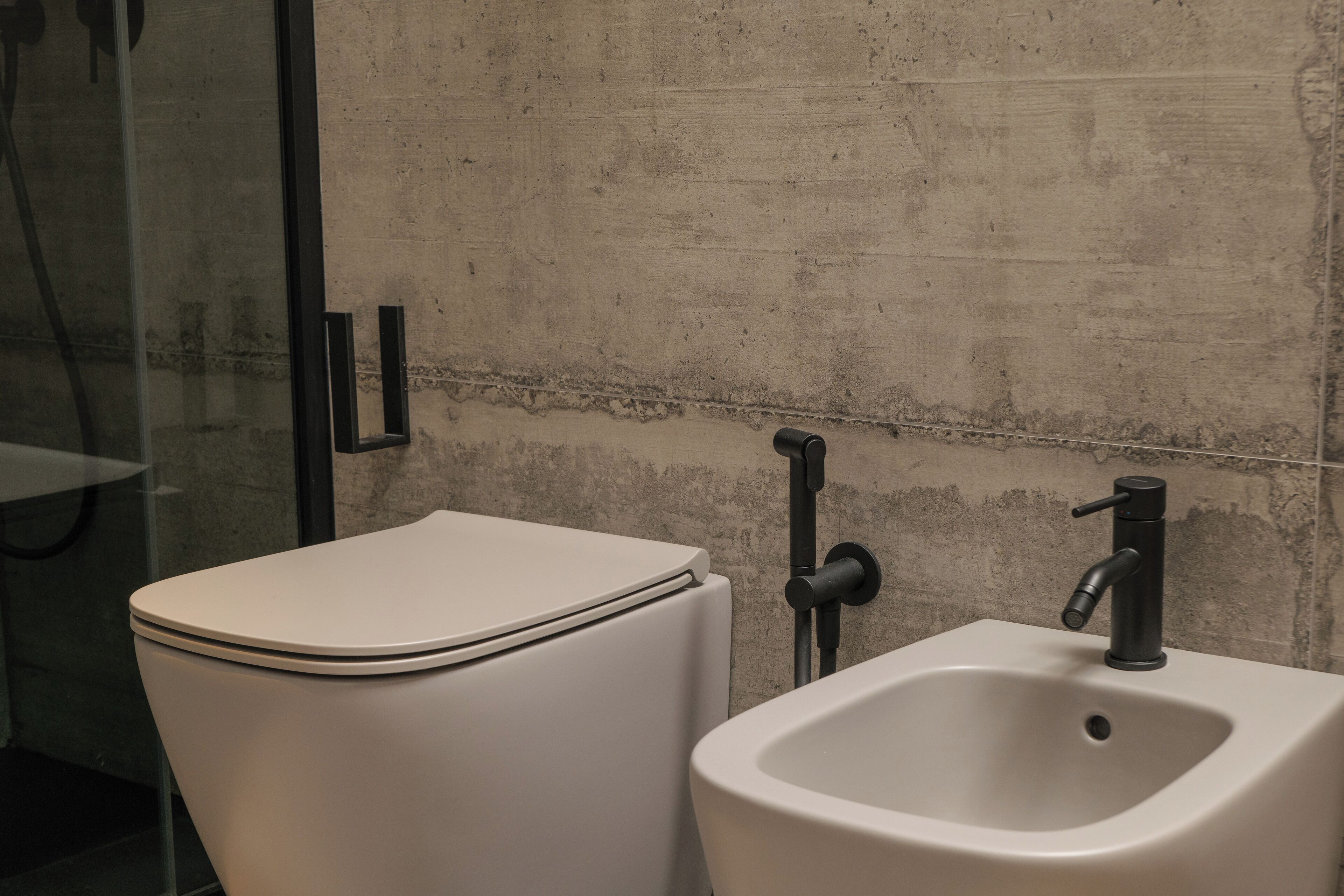 Ein Badezimmer mit Toilette und Waschbecken, beide weiß, an einer strukturierten Wand.