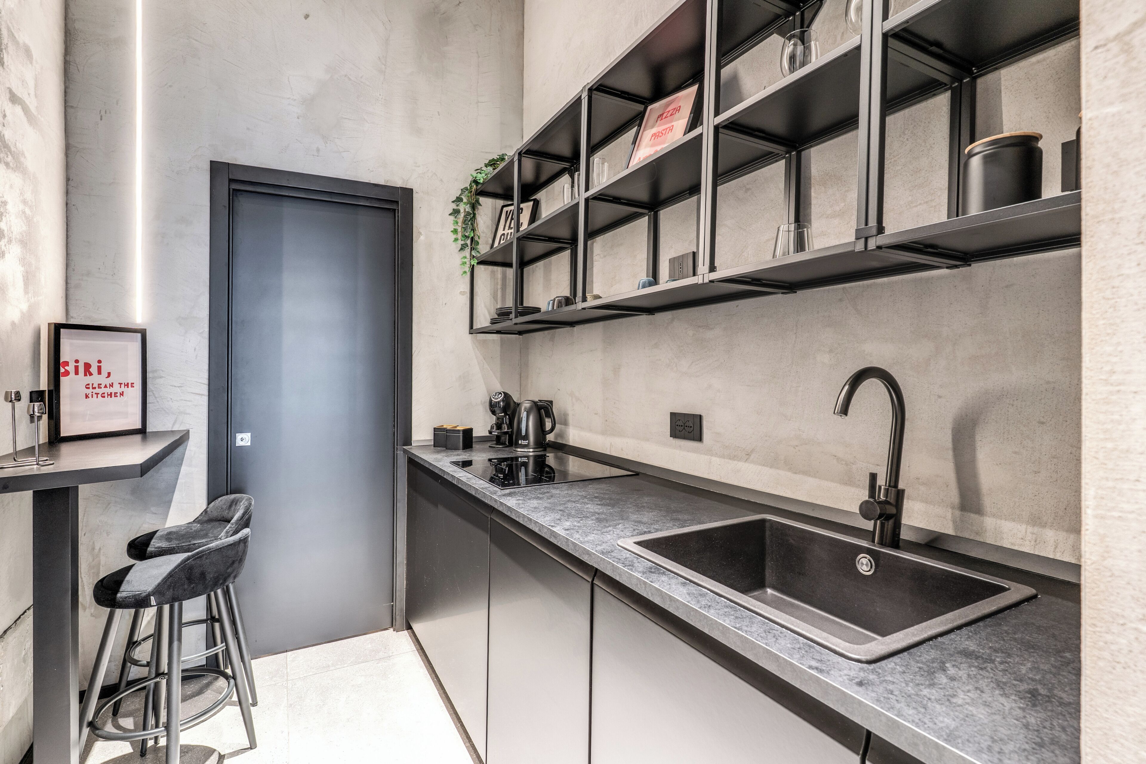 A modern kitchen with a built-in sink, bar stools, and a shelf with kitchen items.