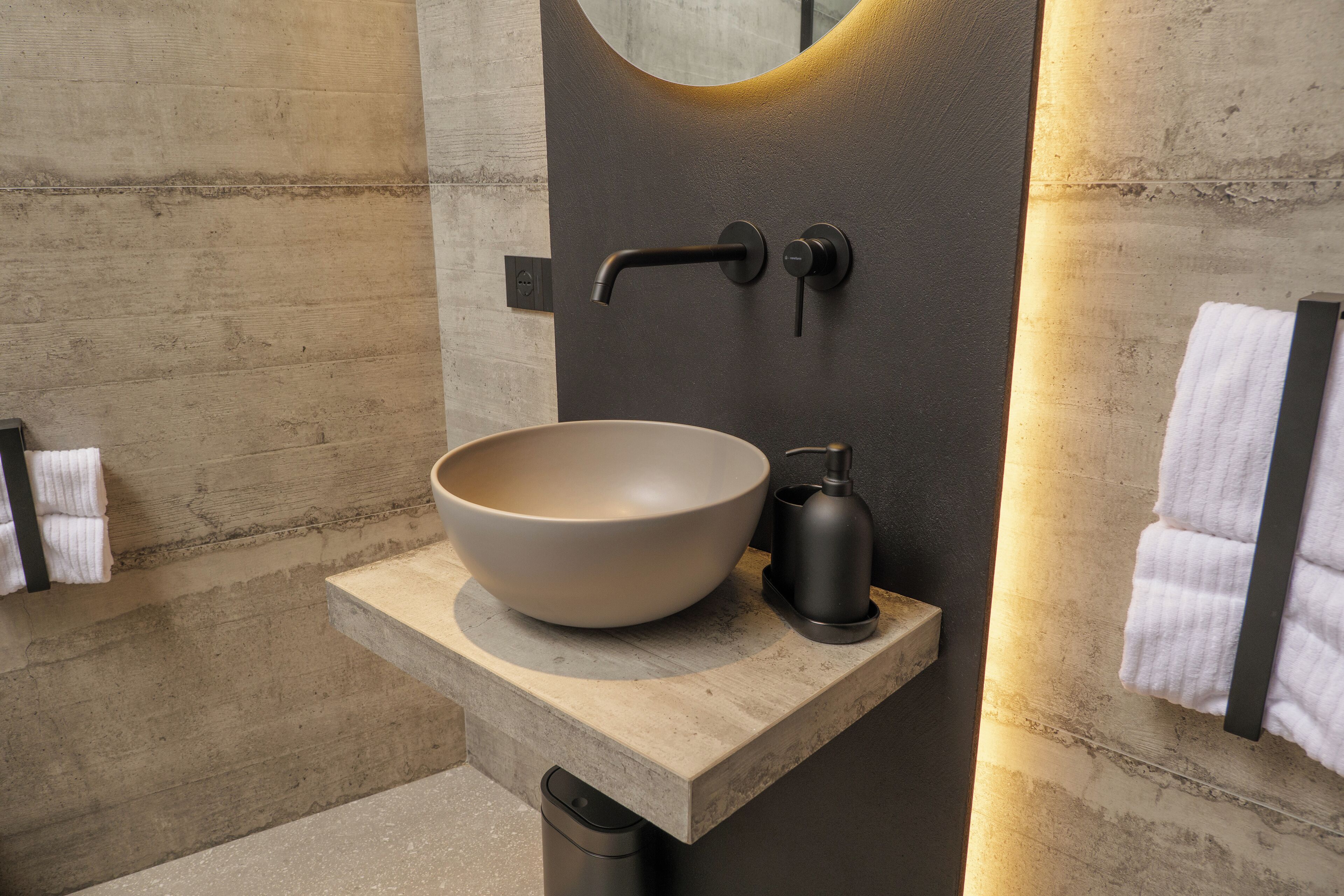 A modern bathroom with a large beige sink, a black faucet, and a soap dispenser on a beige countertop.