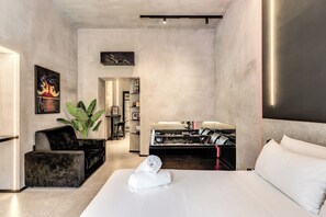 A modern hotel room with a bed, a black sofa, a large plant, and a desk with a computer. - Gallery Home Napoli (Naples)