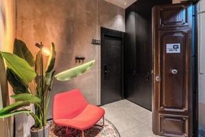 A modern interior with a red chair, a potted plant, and a wooden cabinet with a 'G HOME' sign. - Gallery Home Napoli (Naples)