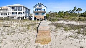 A wooden boardwalk leading to a beachfront property with two multi-story houses, one with a balcony and the other with a covered deck. - Bluebell: Beachfront, Private Pool, Arcade Games, Plantation (St. George Island)